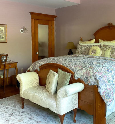 Large king bed with floral comforter, seat at the end of the bed, desk and mirrored closet