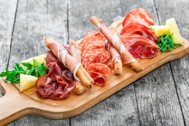 Wooden cutting board with shaved meats and cubed cheeses